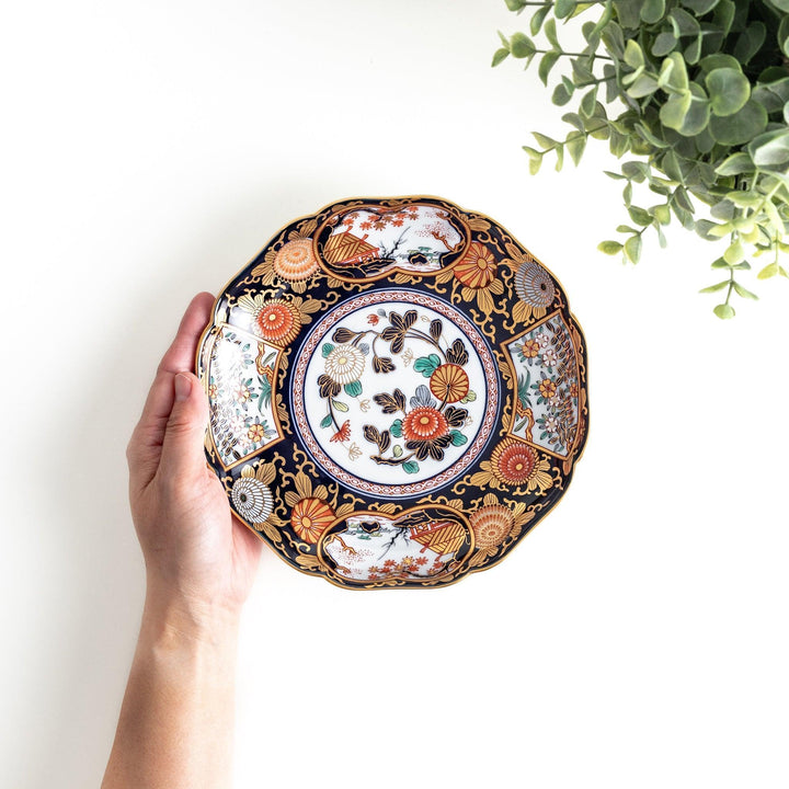 A deep round luncheon plate with a dark blue background, featuring a central floral design and gold accents, surrounded by detailed floral and landscape scenes.