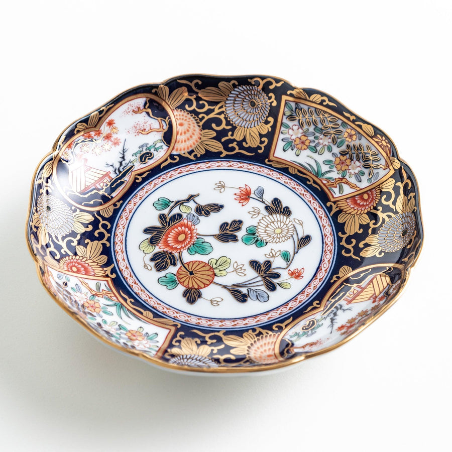 A deep round salad plate with a dark blue background, featuring a central floral design and intricate gold and red patterns with small scenes of Japanese landscapes.