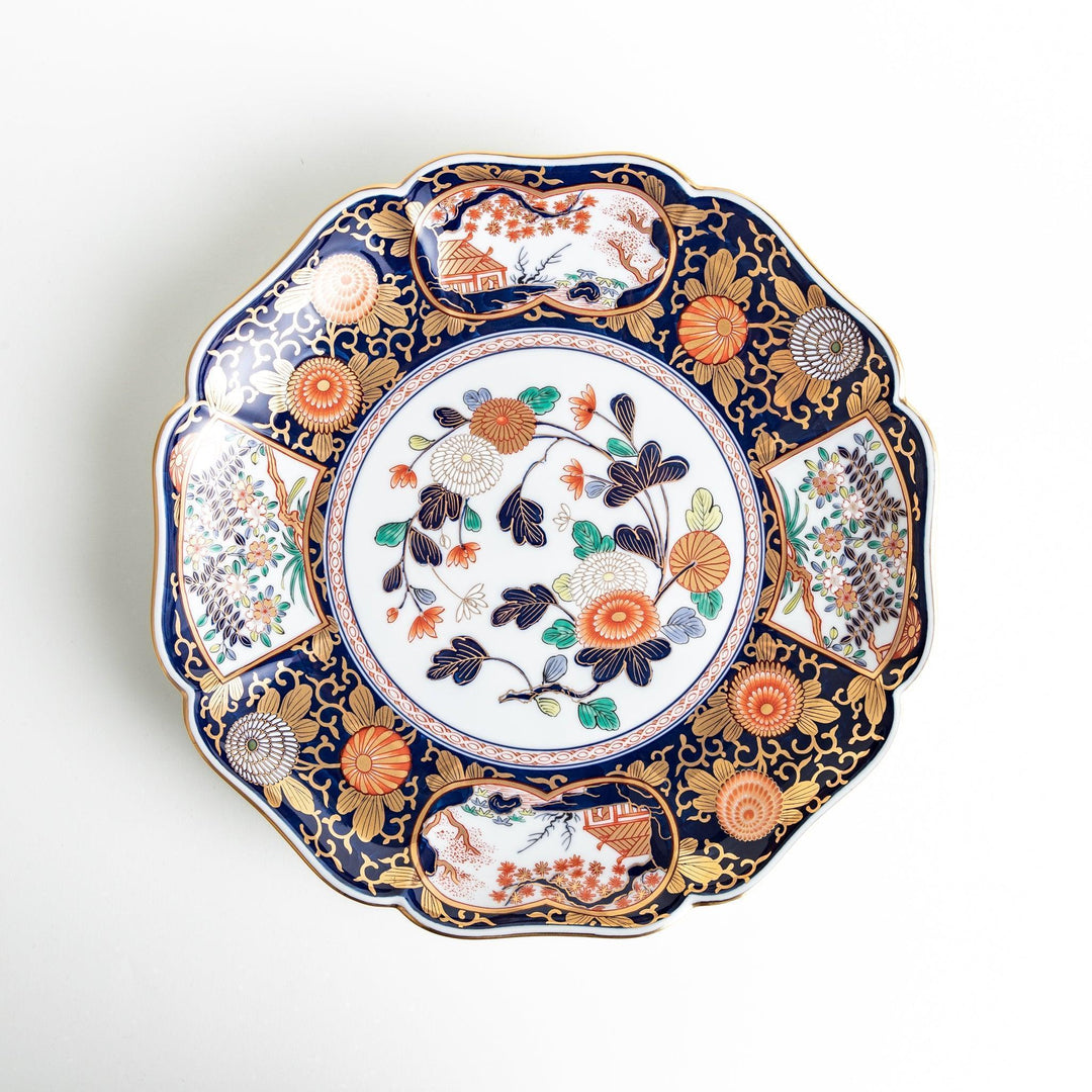 A large round serving plate with a dark blue background, featuring a central floral design surrounded by intricate gold, red, and green patterns and small scenes of Japanese landscapes.