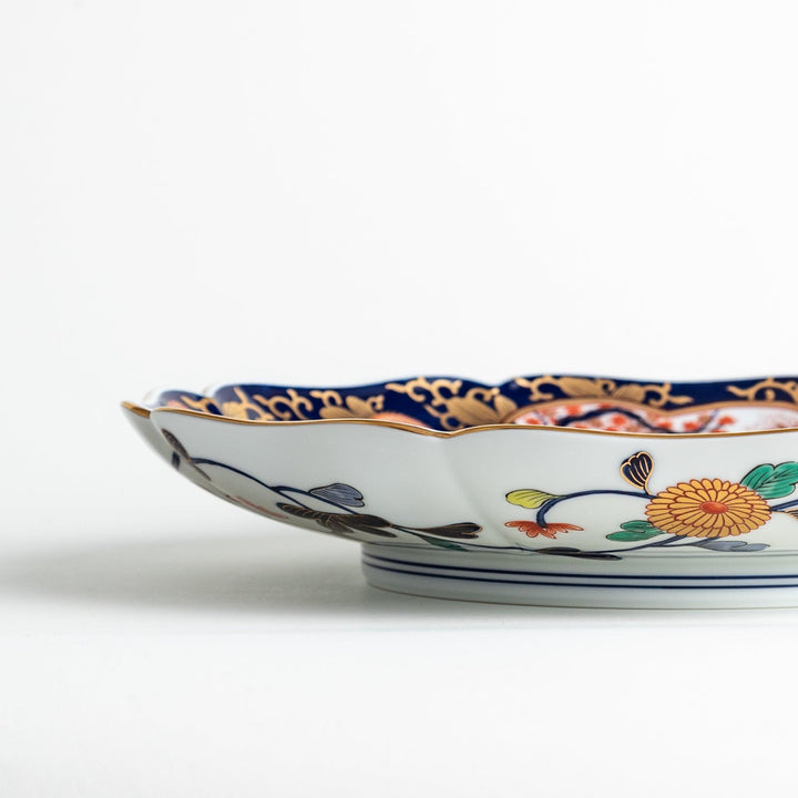 A large round serving plate with a dark blue background, featuring a central floral design surrounded by intricate gold, red, and green patterns and small scenes of Japanese landscapes.