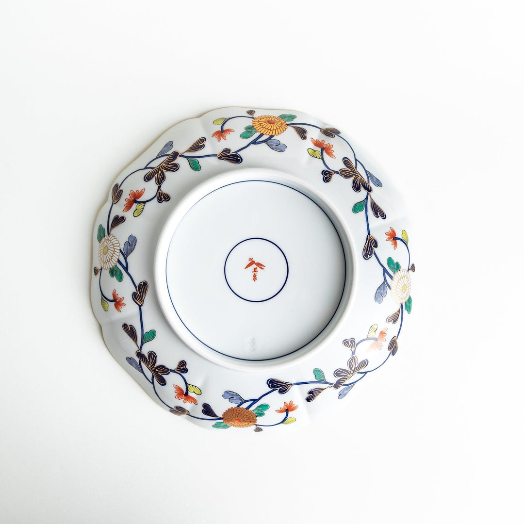 A large round serving plate with a dark blue background, featuring a central floral design surrounded by intricate gold, red, and green patterns and small scenes of Japanese landscapes.