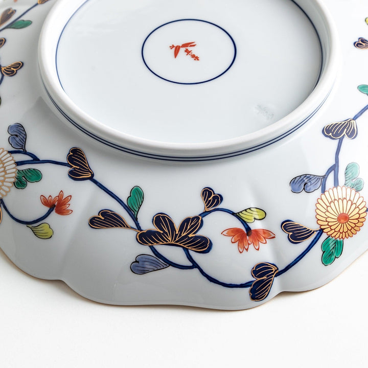 A large round serving plate with a dark blue background, featuring a central floral design surrounded by intricate gold, red, and green patterns and small scenes of Japanese landscapes.