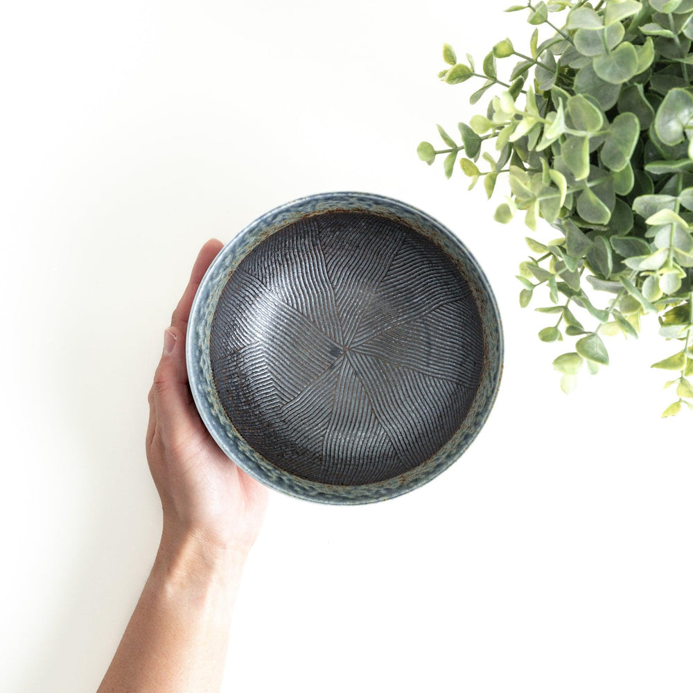 A bowl with a textured glaze featuring a mix of blue, brown, and cream colors with a ridged interior.