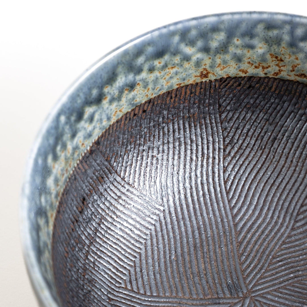 A bowl with a textured glaze featuring a mix of blue, brown, and cream colors with a ridged interior.