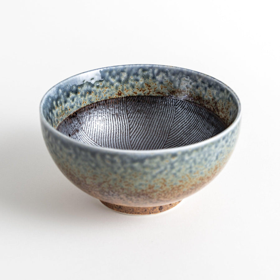 A bowl with a textured glaze featuring a mix of blue, brown, and cream colors with a ridged interior.