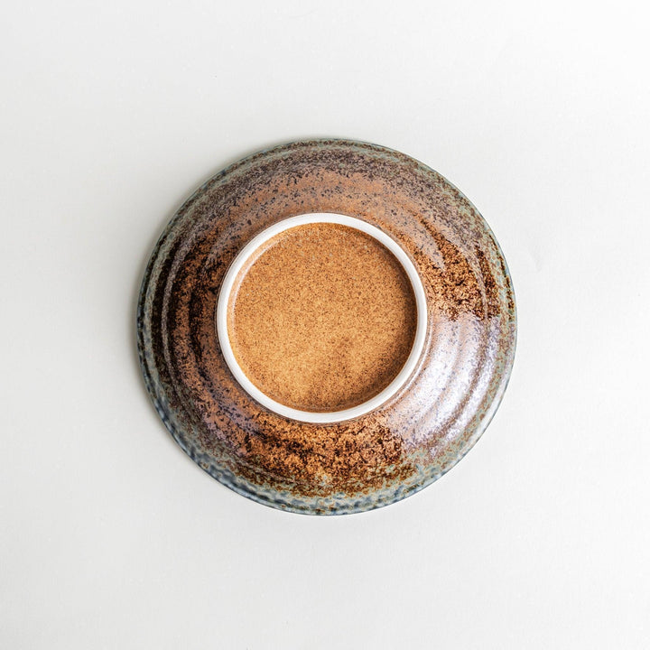 A pasta bowl with a textured glaze in blue, brown, and cream hues, featuring a ridged interior.