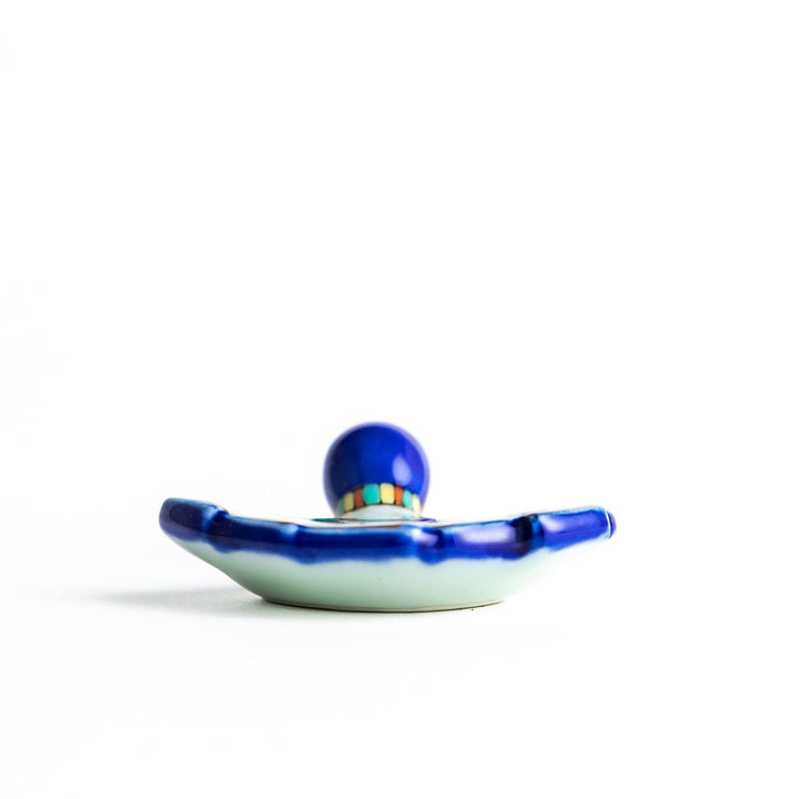 A fan-shaped ceramic chopstick rest decorated with a bird, flowers, and leaves in vibrant colors, with a blue handle.