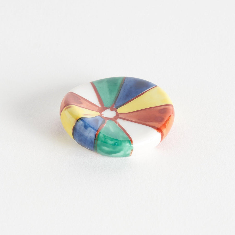 A colorful round ceramic chopstick rest with a pinwheel design.