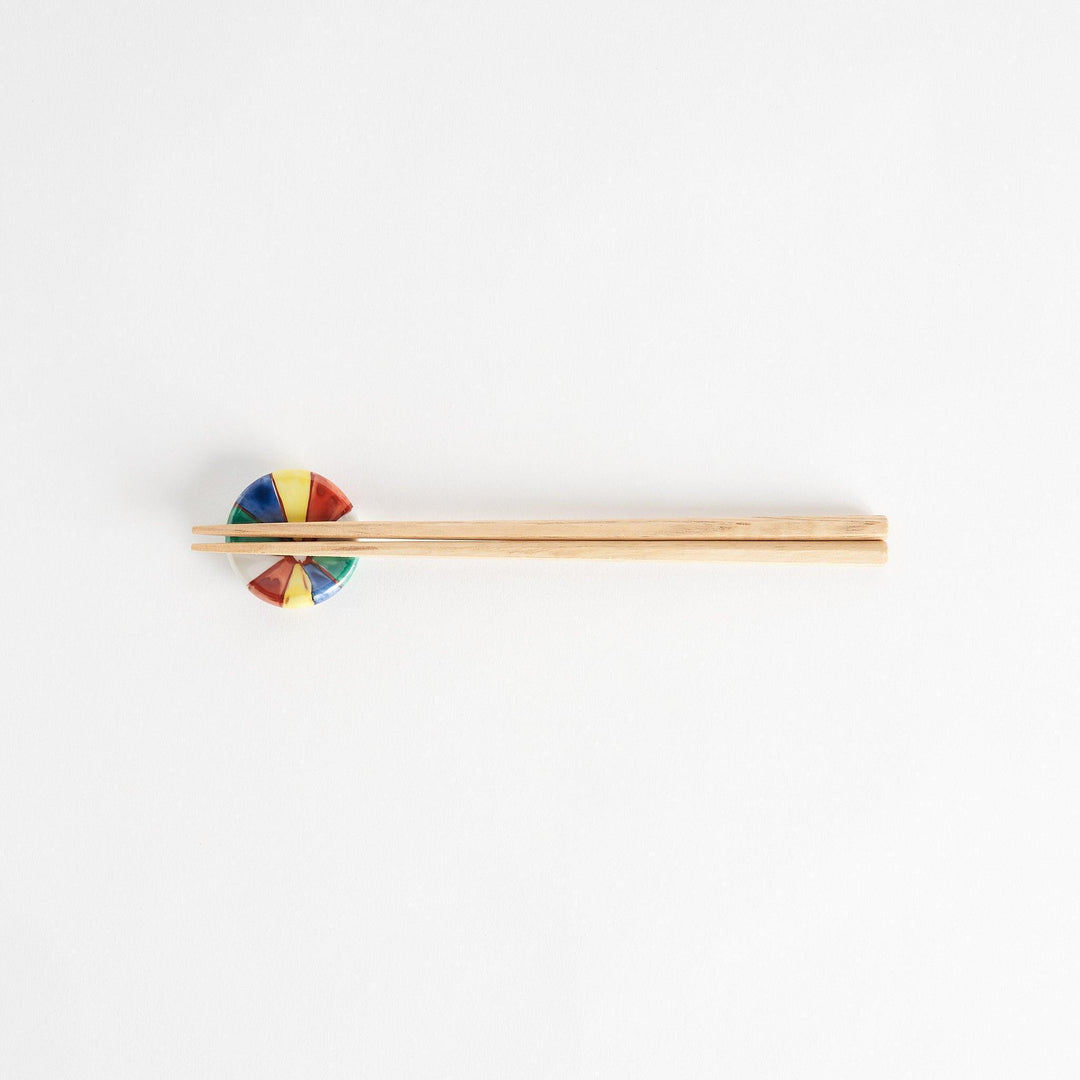 A colorful round ceramic chopstick rest with a pinwheel design.