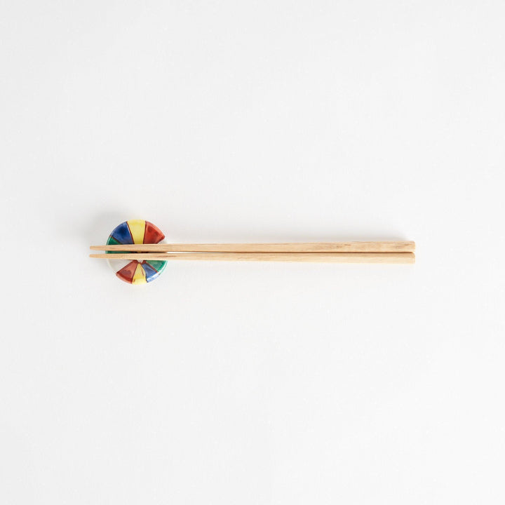 A colorful round ceramic chopstick rest with a pinwheel design.