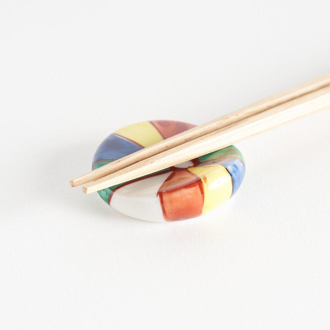 A colorful round ceramic chopstick rest with a pinwheel design.