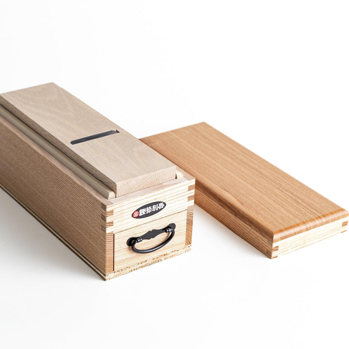 A large wooden box with a sliding drawer and lid, designed for shaving katsuobushi (dried bonito), with a colorful packaging box featuring traditional Japanese artwork.