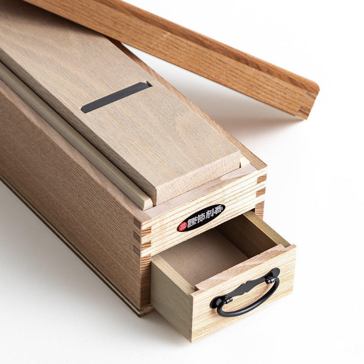 A large wooden box with a sliding drawer and lid, designed for shaving katsuobushi (dried bonito), with a colorful packaging box featuring traditional Japanese artwork.