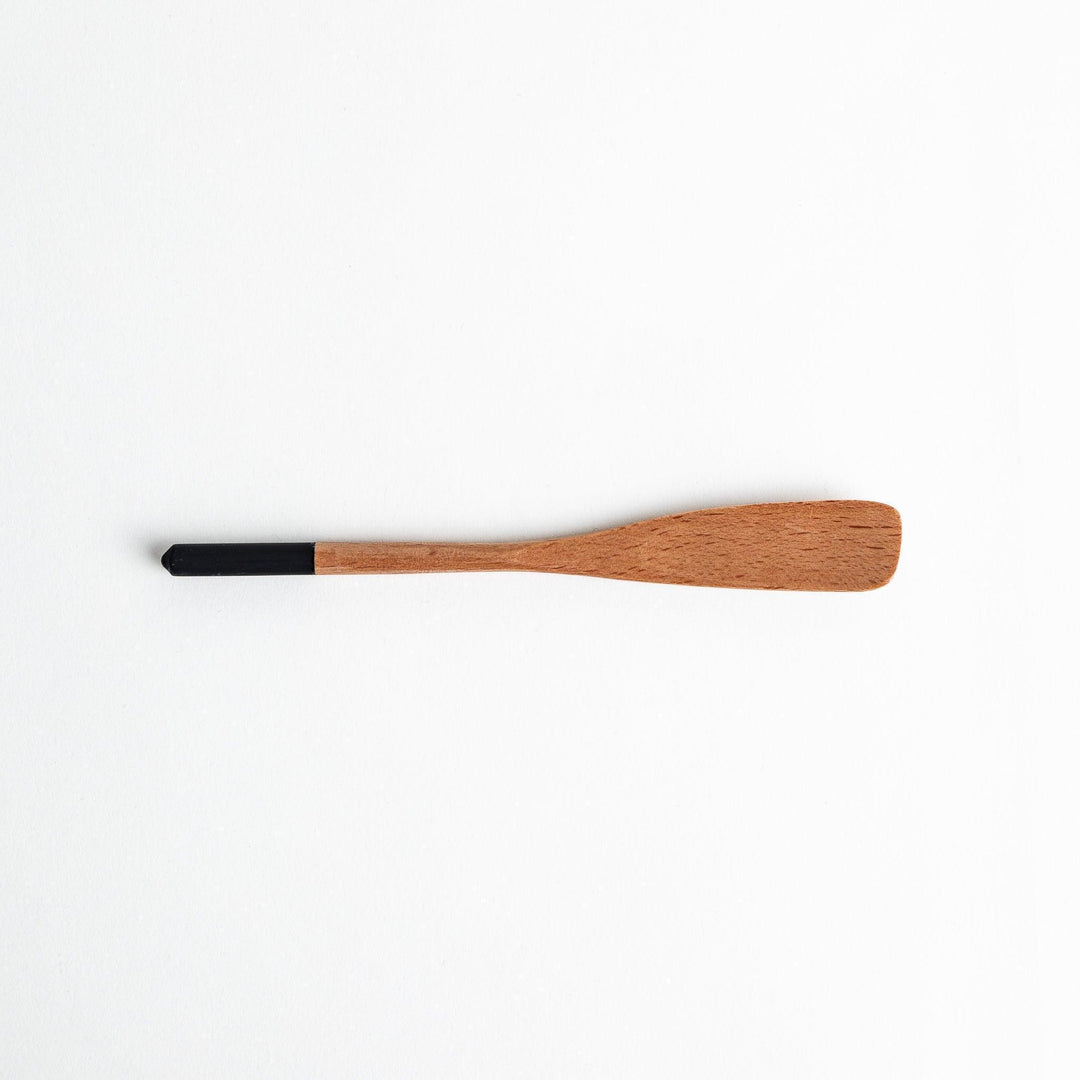 A set of four wooden spatulas with flat tips, each featuring a different colored end—white, black, blue, and red