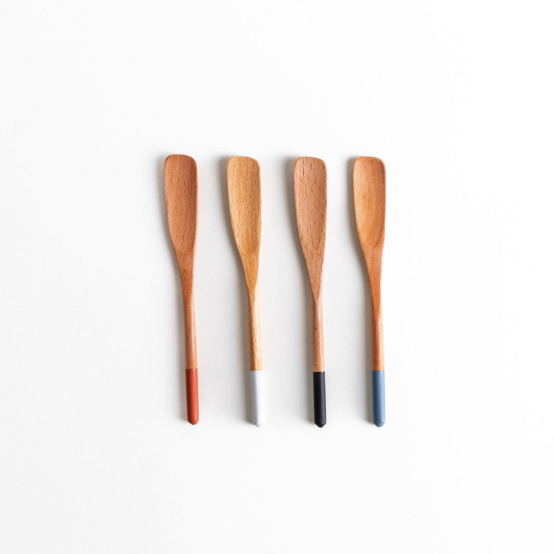 A set of four wooden spatulas with flat tips, each featuring a different colored end—white, black, blue, and red