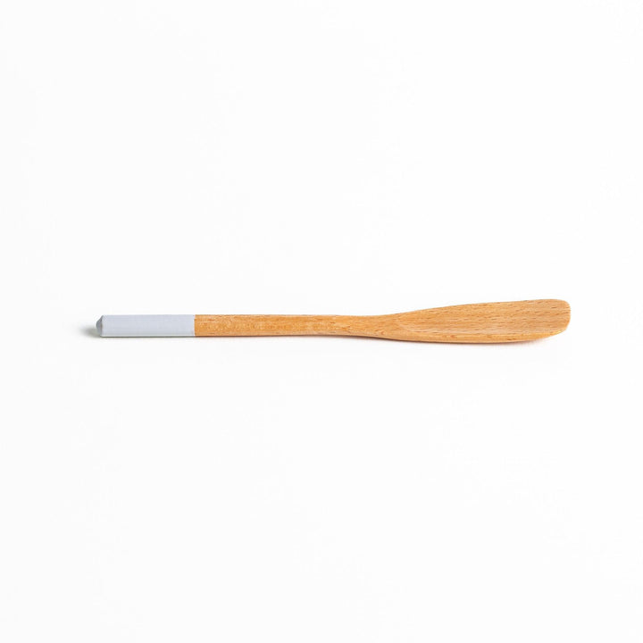 A set of four wooden spatulas with flat tips, each featuring a different colored end—white, black, blue, and red