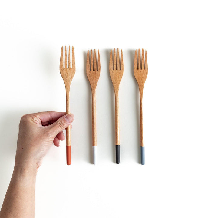 A set of four wooden pasta fork, each with a different colored tip—white, black, blue, and red.