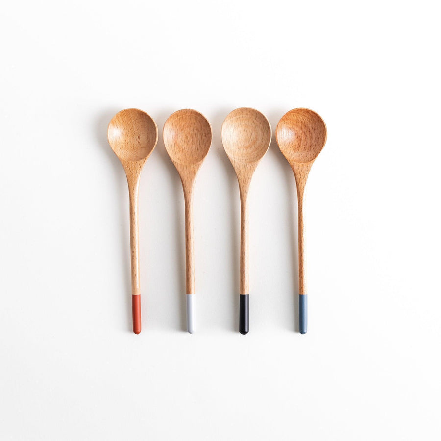 A set of four wooden soup spoons with wide, rounded bowls and colored tips—white, black, blue, and red.