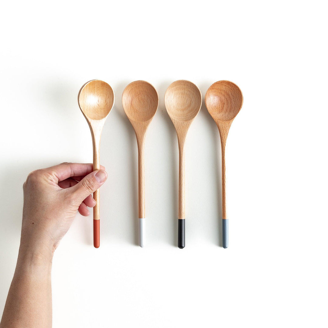 A set of four wooden soup spoons with wide, rounded bowls and colored tips—white, black, blue, and red.