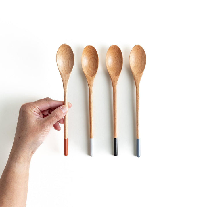 A set of four wooden curry spoons, each with a different colored tip—white, black, blue, and red.