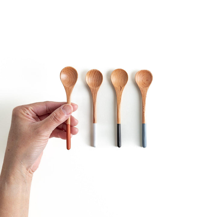 A set of four wooden tea spoons with wide, rounded bowls and colored tips—white, black, blue, and red.