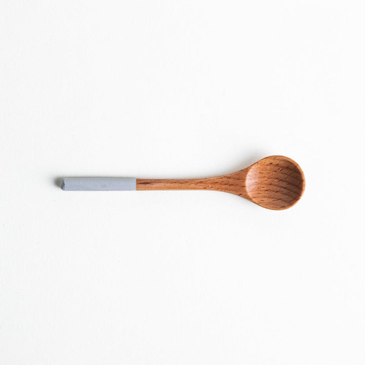 A set of four wooden tea spoons with wide, rounded bowls and colored tips—white, black, blue, and red.