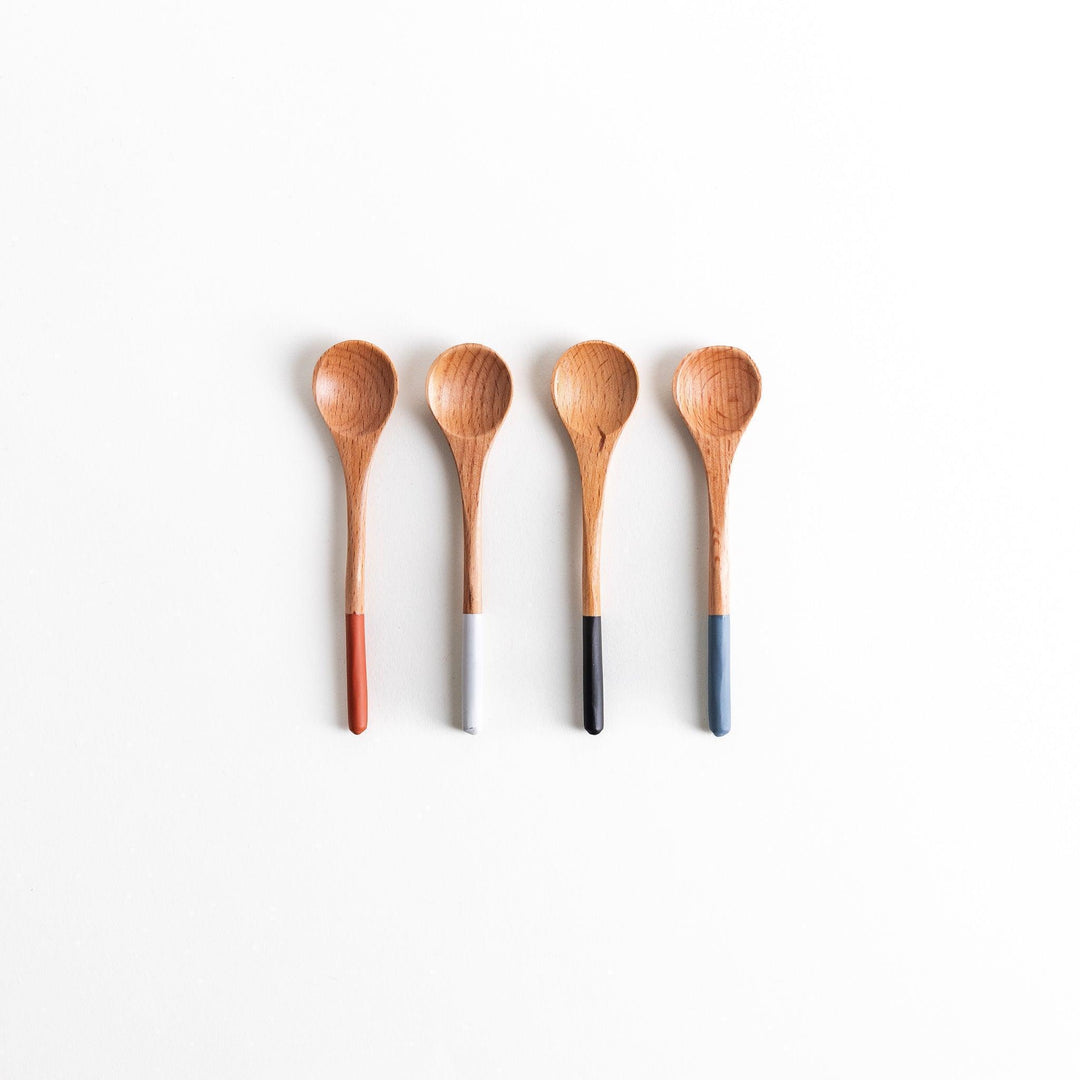 A set of four wooden tea spoons with wide, rounded bowls and colored tips—white, black, blue, and red.