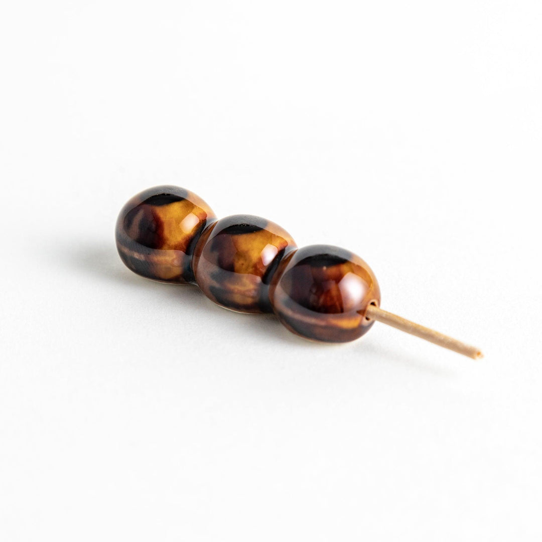 Ceramic chopstick rests shaped like Japanese dango skewers with with three brown balls.