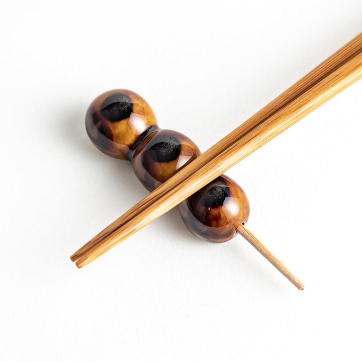 Ceramic chopstick rests shaped like Japanese dango skewers with with three brown balls.