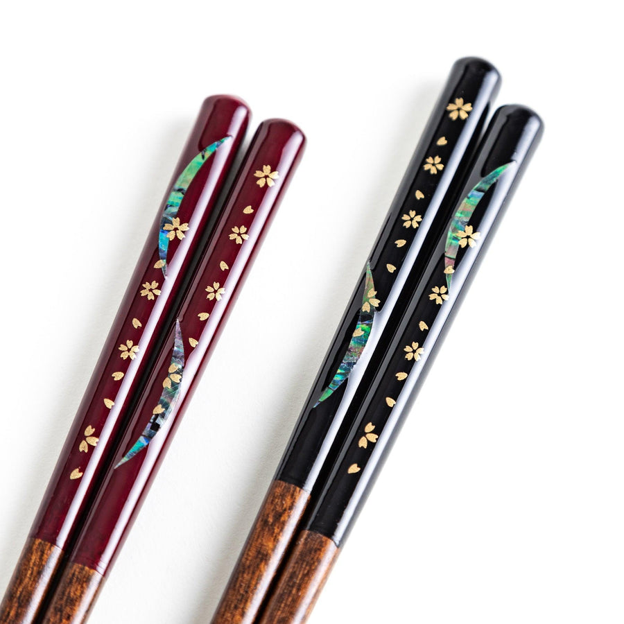 Two pairs of chopsticks, one with red and one with black handles, featuring moon and sakura design.