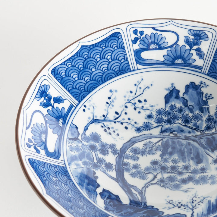 A bowl with a dark blue exterior and a white interior adorned with floral and wave patterns in blue and landscape in the cetner.