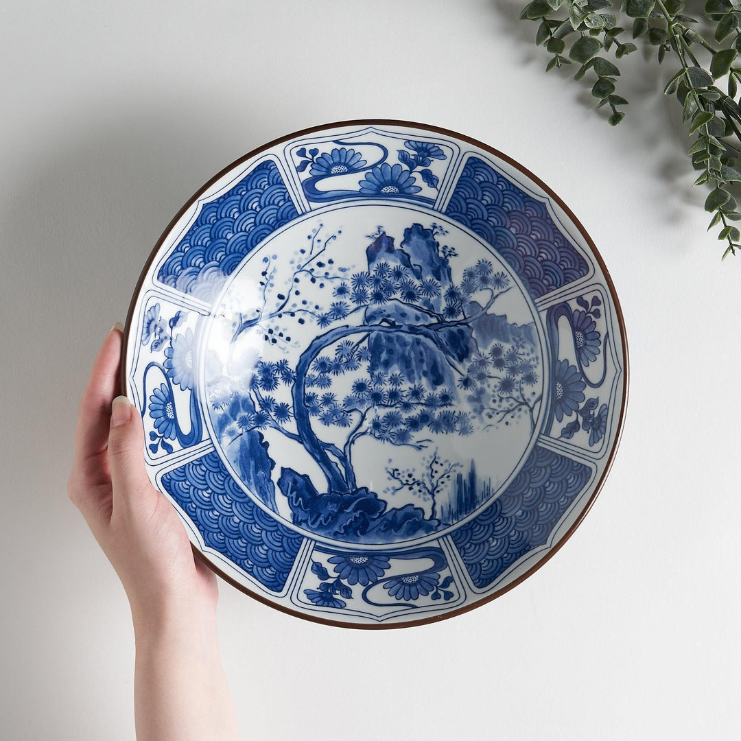 A bowl with a dark blue exterior and a white interior adorned with floral and wave patterns in blue and landscape in the cetner.