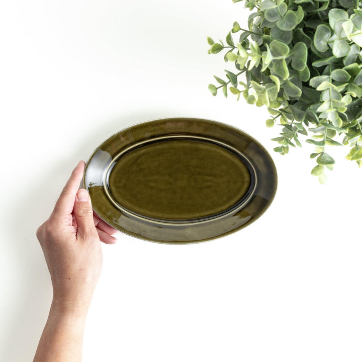 Sleek, dark brown or olive colored oval salad plate with a glossy finish, simple and minimalist.