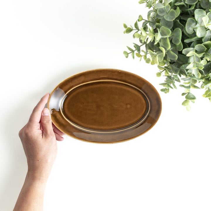 Sleek, dark brown or olive colored oval salad plate with a glossy finish, simple and minimalist.