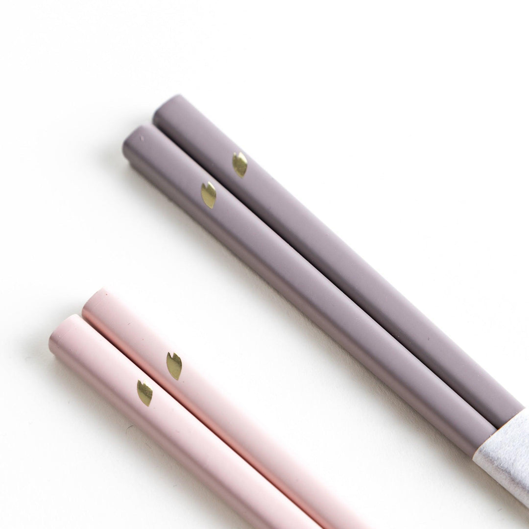 Set of two pairs of chopsticks with wooden handles, one pair in a pale gray color and the other in a light pink, presented with glass chopstick rests in a wooden gift box.