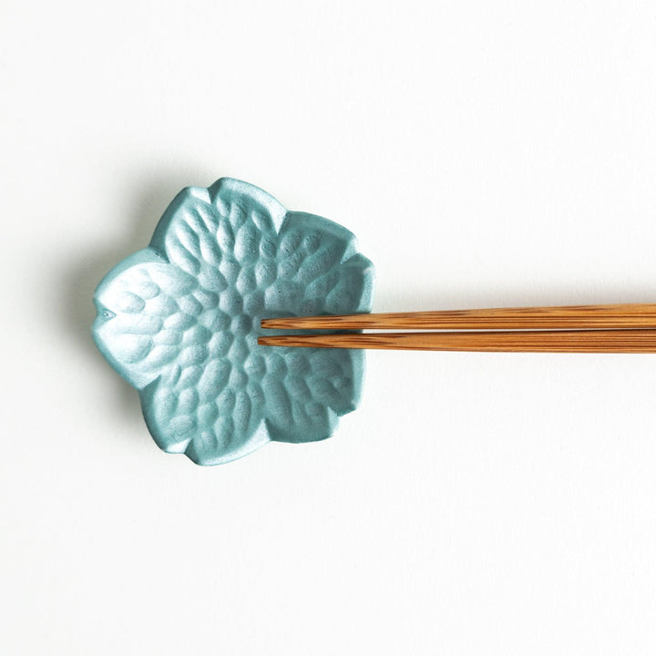 Small, flower-shaped chipsticks rest in different colors: yellow, blue, white, and pink, arranged in a square formation on a wooden surface.