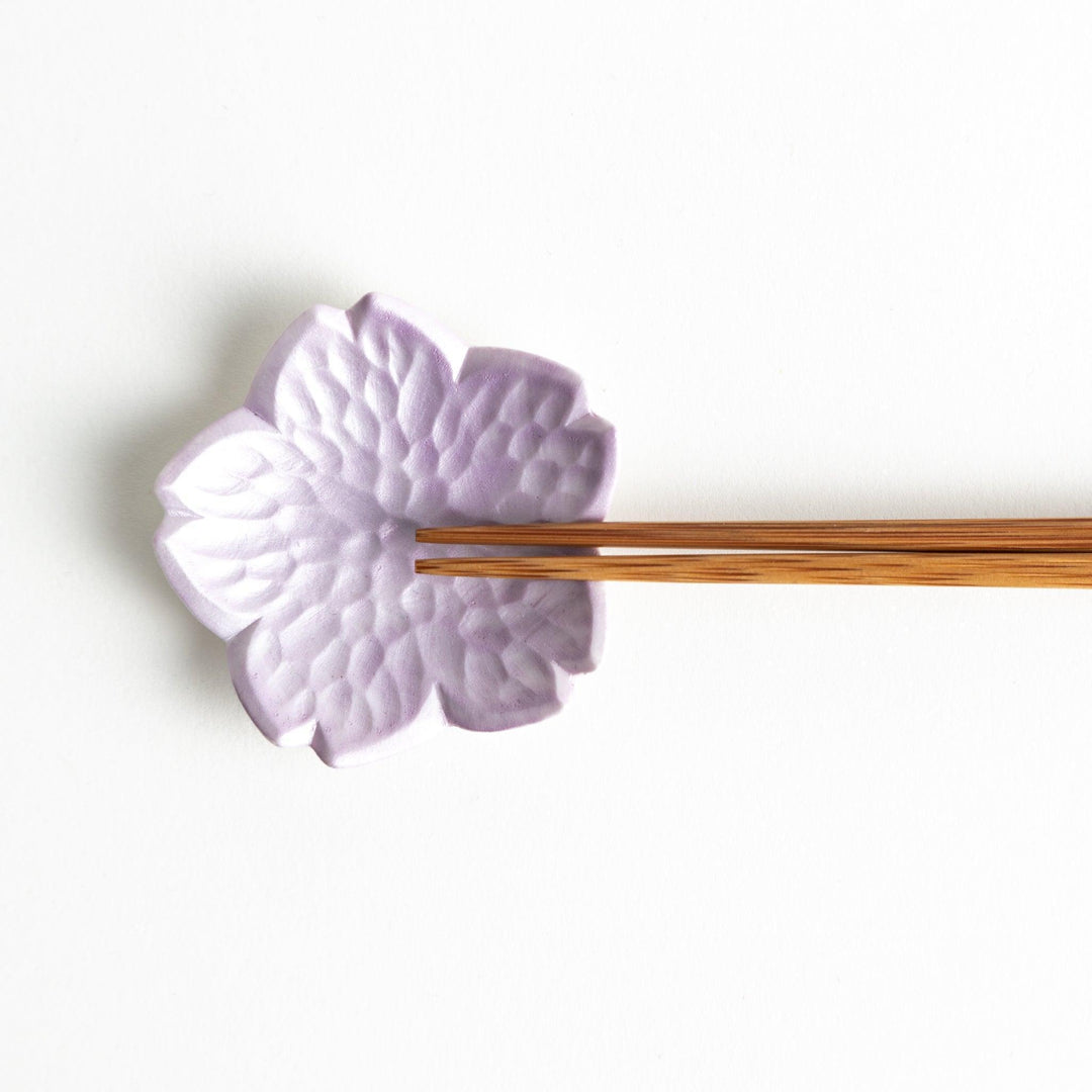 Small, flower-shaped chipsticks rest in different colors: yellow, blue, white, and pink, arranged in a square formation on a wooden surface.