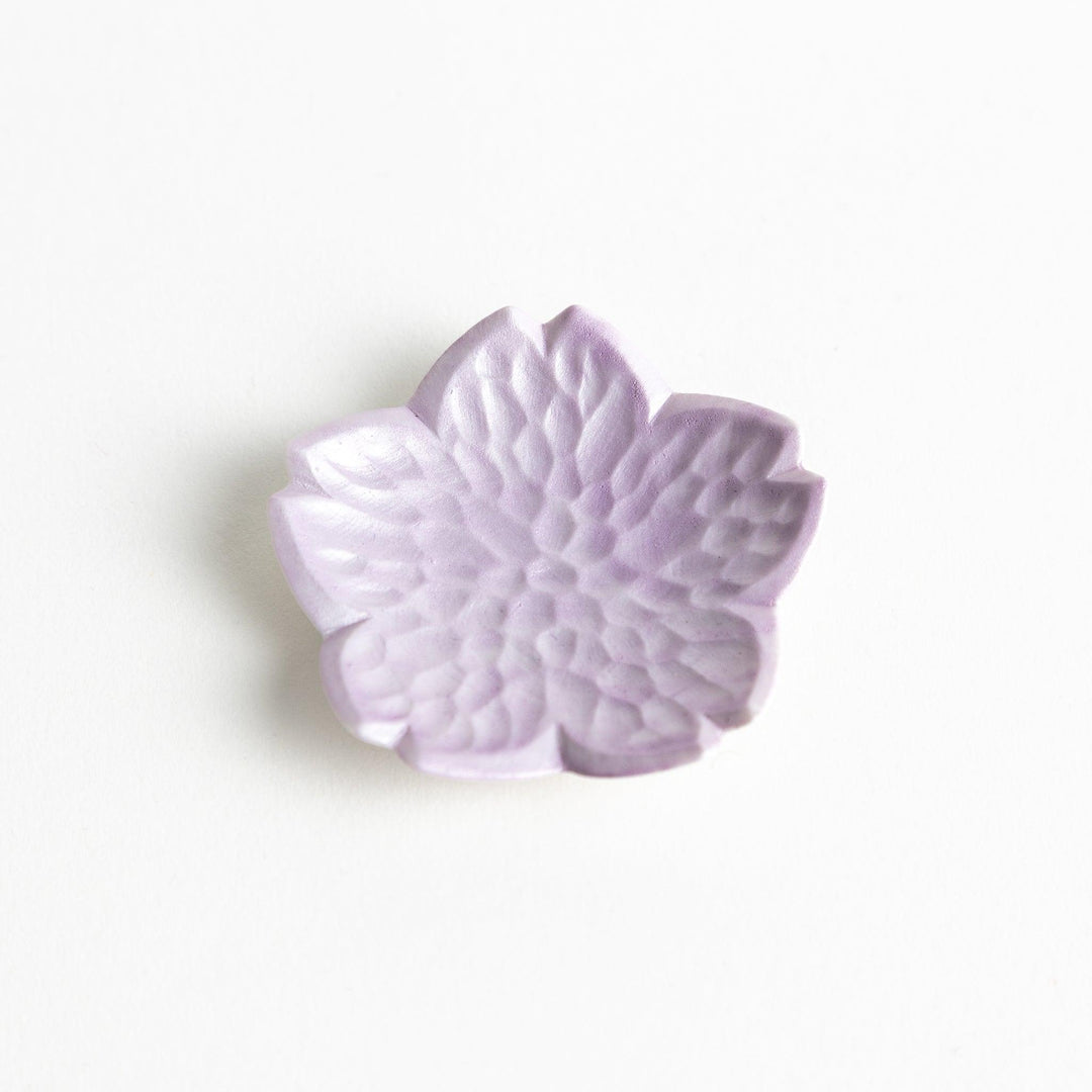 Small, flower-shaped chipsticks rest in different colors: yellow, blue, white, and pink, arranged in a square formation on a wooden surface.