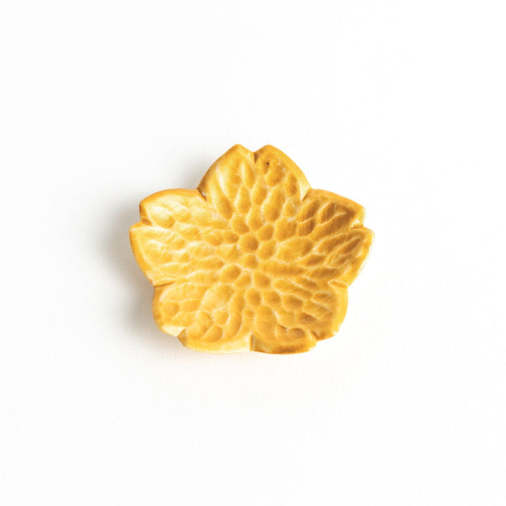 Small, flower-shaped chipsticks rest in different colors: yellow, blue, white, and pink, arranged in a square formation on a wooden surface.