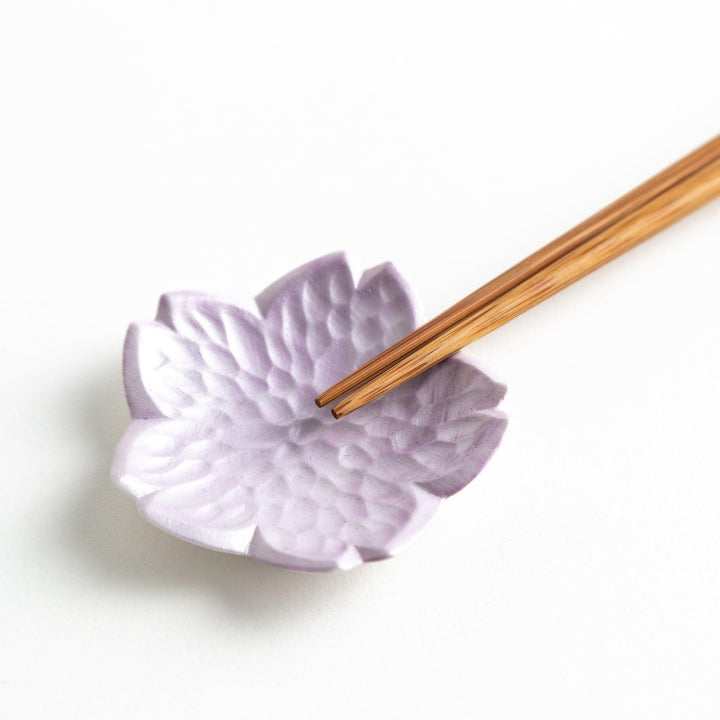 Small, flower-shaped chipsticks rest in different colors: yellow, blue, white, and pink, arranged in a square formation on a wooden surface.