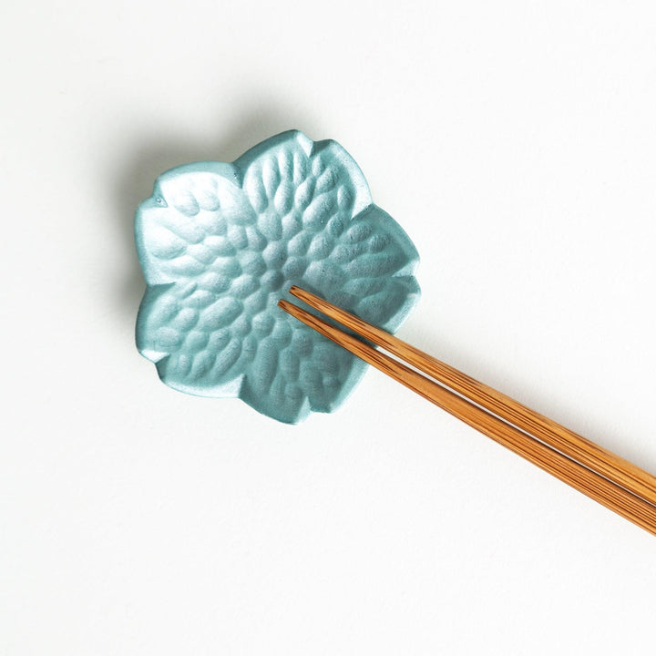 Small, flower-shaped chipsticks rest in different colors: yellow, blue, white, and pink, arranged in a square formation on a wooden surface.