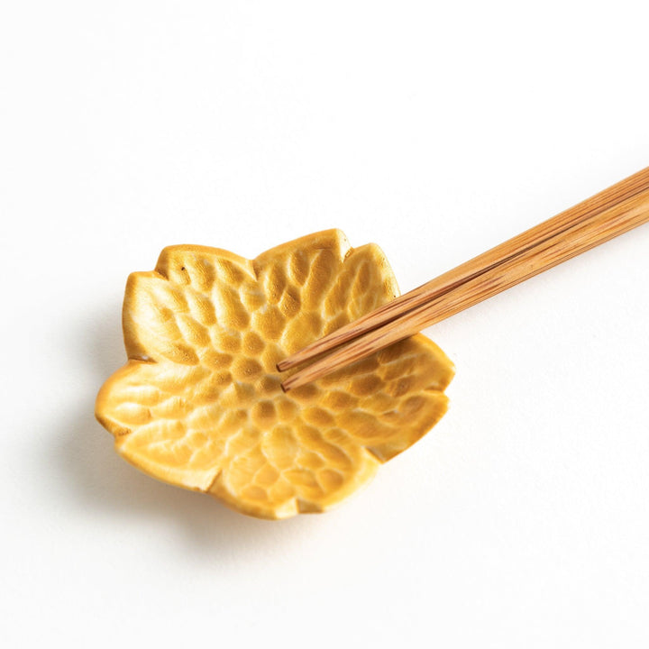 Small, flower-shaped chipsticks rest in different colors: yellow, blue, white, and pink, arranged in a square formation on a wooden surface.