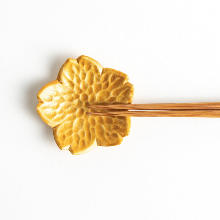 Small, flower-shaped chipsticks rest in different colors: yellow, blue, white, and pink, arranged in a square formation on a wooden surface.