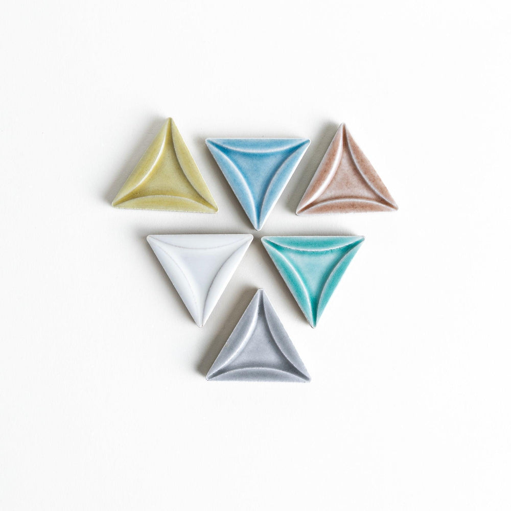 Five small, triangular ceramic chopstick rests in pastel colors—green, brown, blue, turquoise, and gray, arranged randomly on a white background.