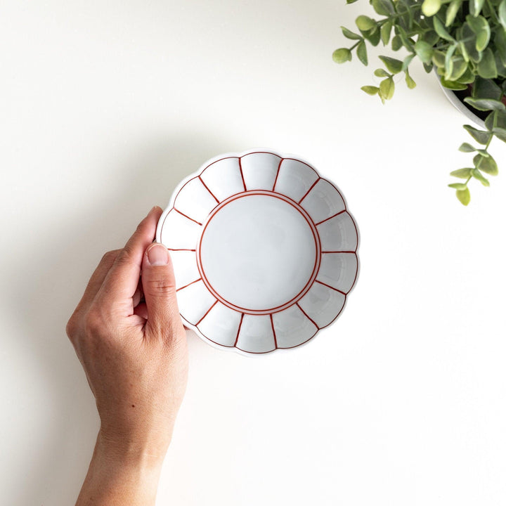 A small white porcelain dessert bowl with delicate blue or red lines radiating from the center, creating a simple yet elegant design.