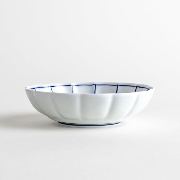 A small white porcelain dessert bowl with delicate blue or red lines radiating from the center, creating a simple yet elegant design.