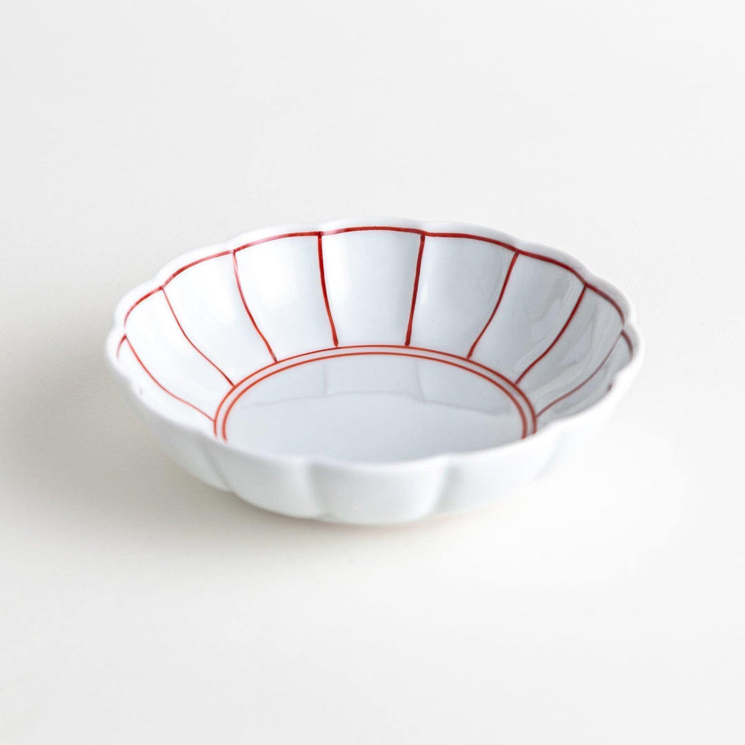 A small white porcelain dessert bowl with delicate blue or red lines radiating from the center, creating a simple yet elegant design.