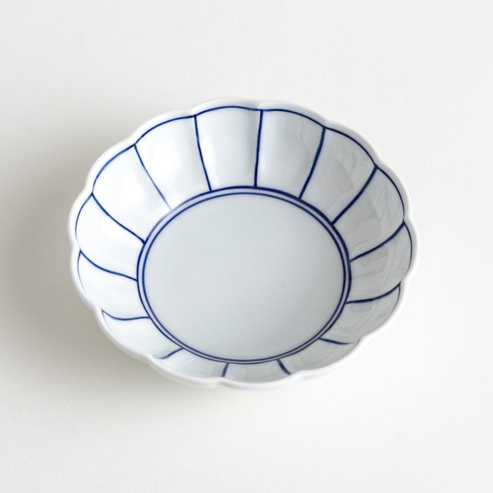 A small white porcelain dessert bowl with delicate blue or red lines radiating from the center, creating a simple yet elegant design.