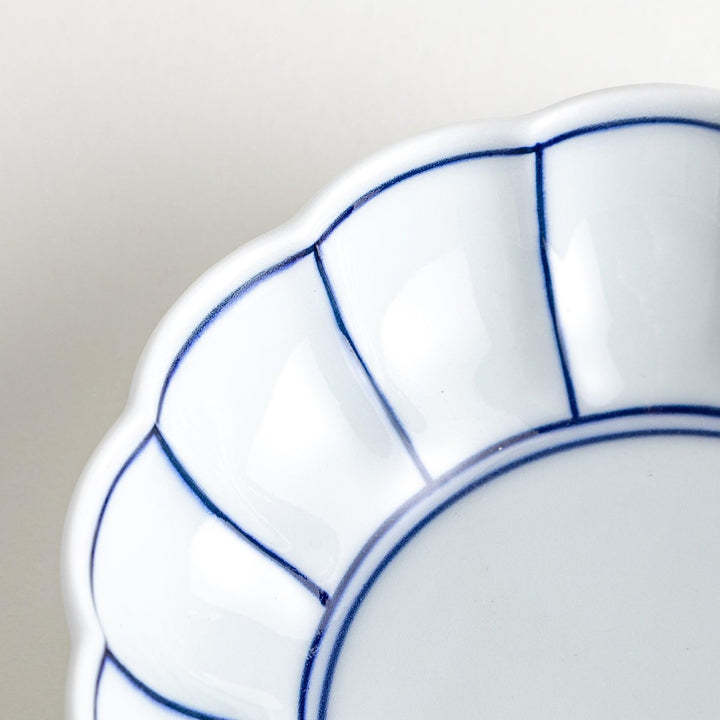 A small white porcelain dessert bowl with delicate blue or red lines radiating from the center, creating a simple yet elegant design.