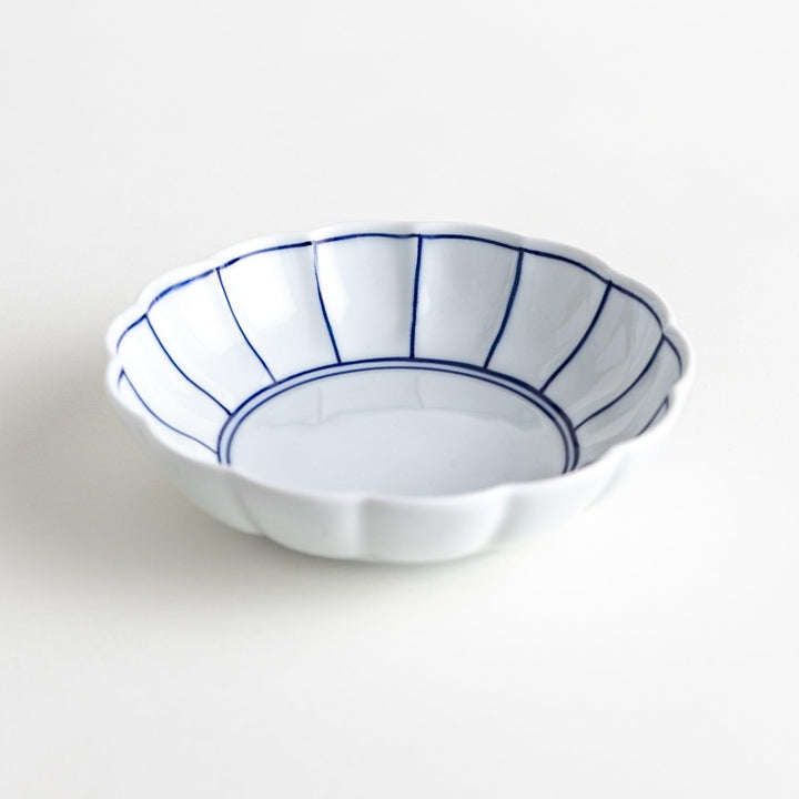 A small white porcelain dessert bowl with delicate blue or red lines radiating from the center, creating a simple yet elegant design.